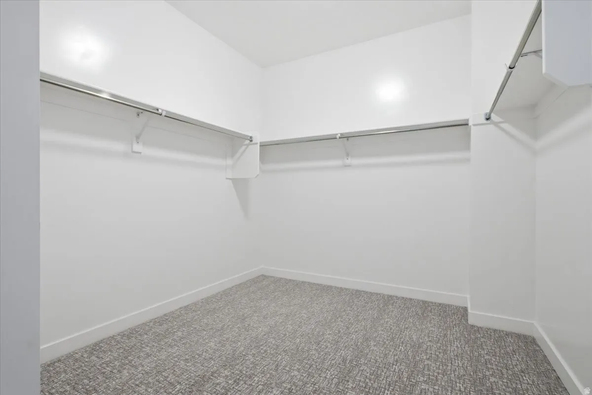 Spacious walk-in closet featuring light gray patterned carpeting, white walls, white baseboards, and built-in chrome hanging rods with shelving