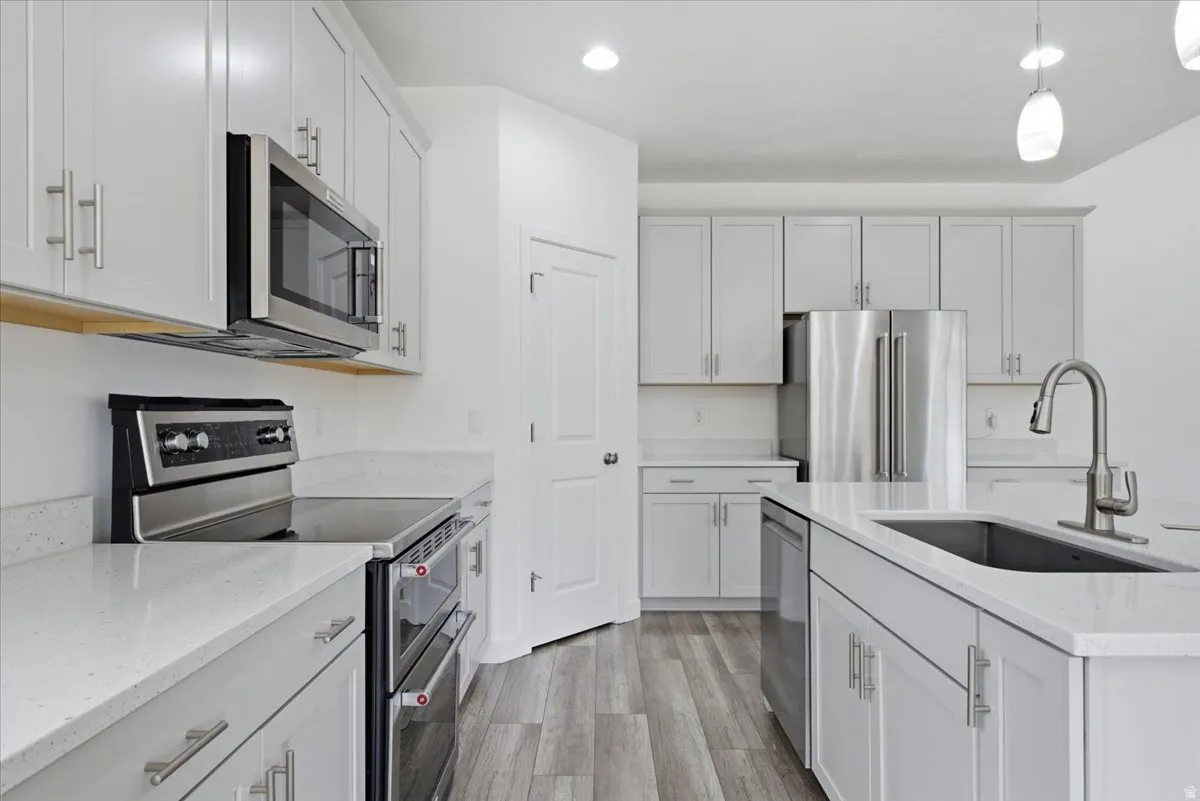 Contemporary kitchen featuring light gray cabinetry, stainless steel appliances, white countertops, a central island with an undermount sink, and wood-finish flooring