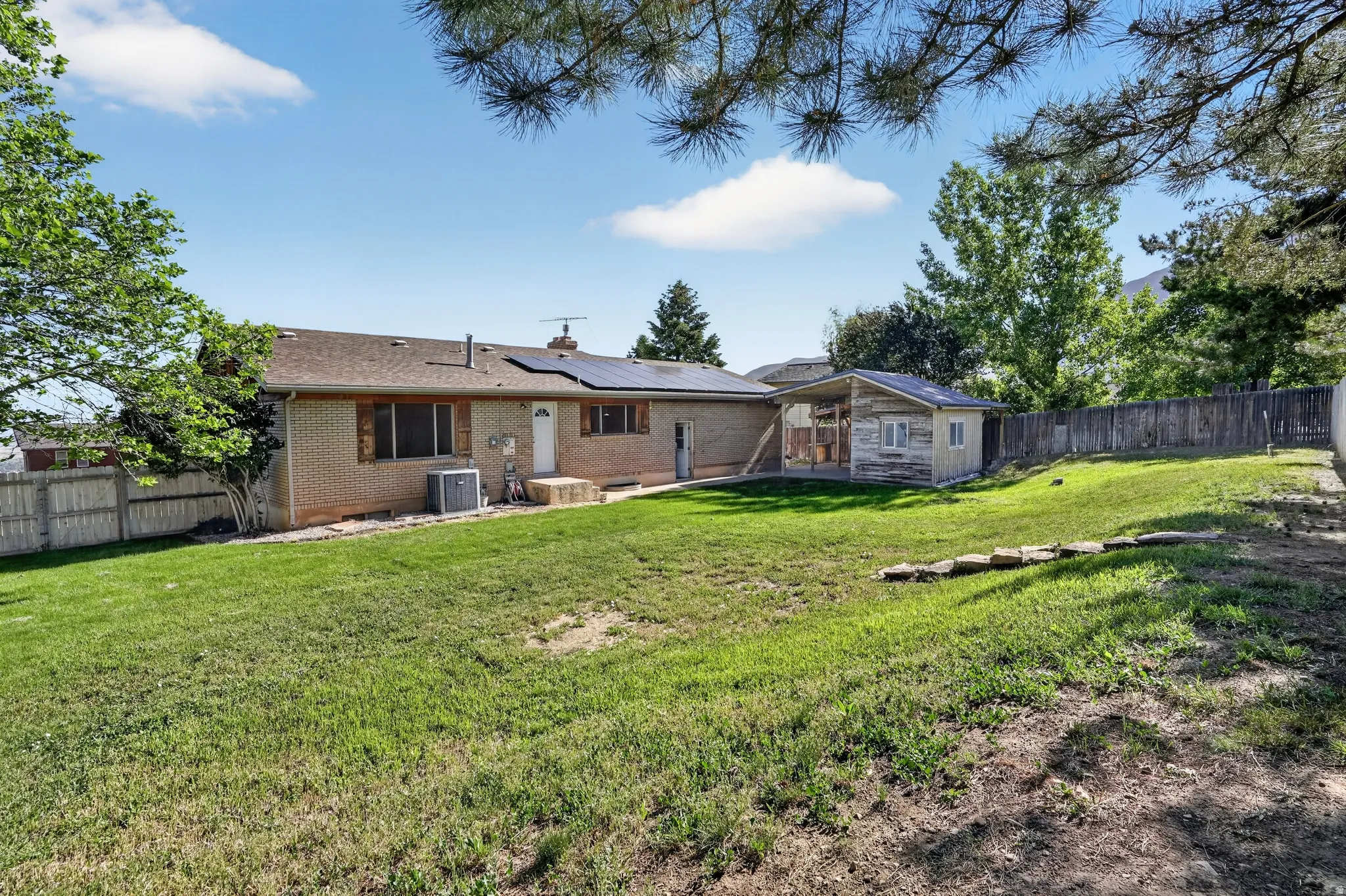 Expansive grassy yard featuring a brick exterior, solar panels, and a detached shed