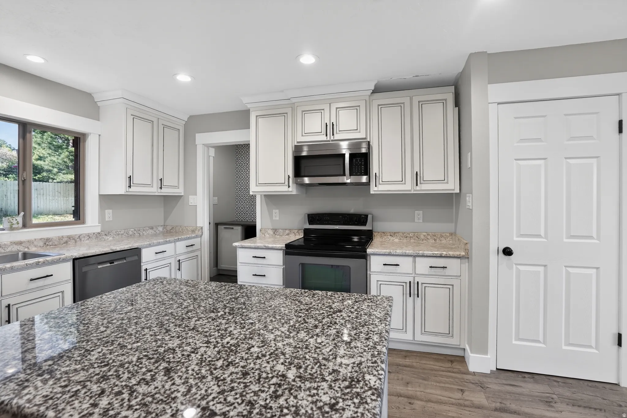 Kitchen featuring a large island with a speckled countertop, white cabinetry with dark hardware, stainless steel appliances, and wood-finish flooring