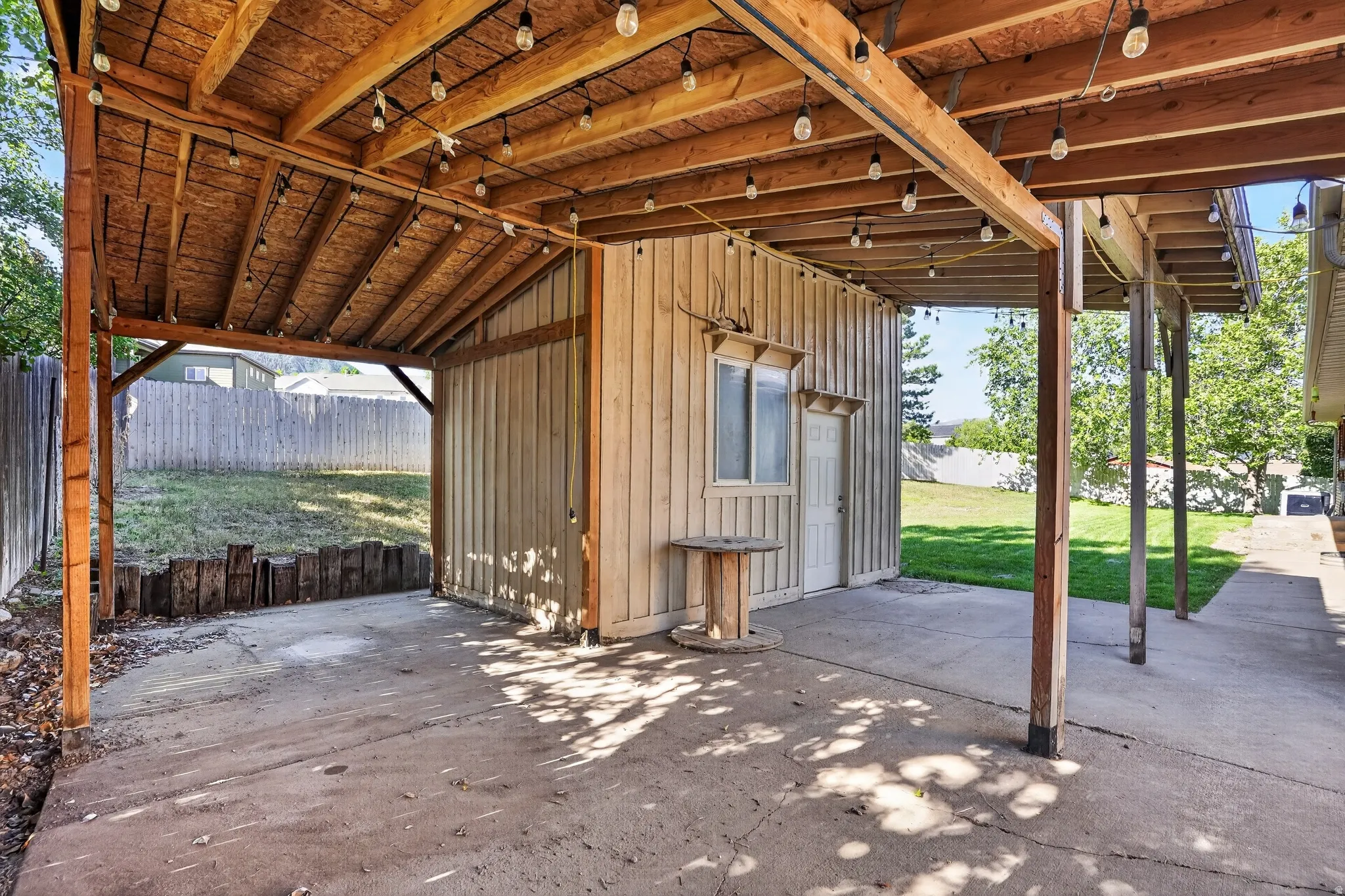 Covered concrete patio featuring exposed wood beams and string lighting