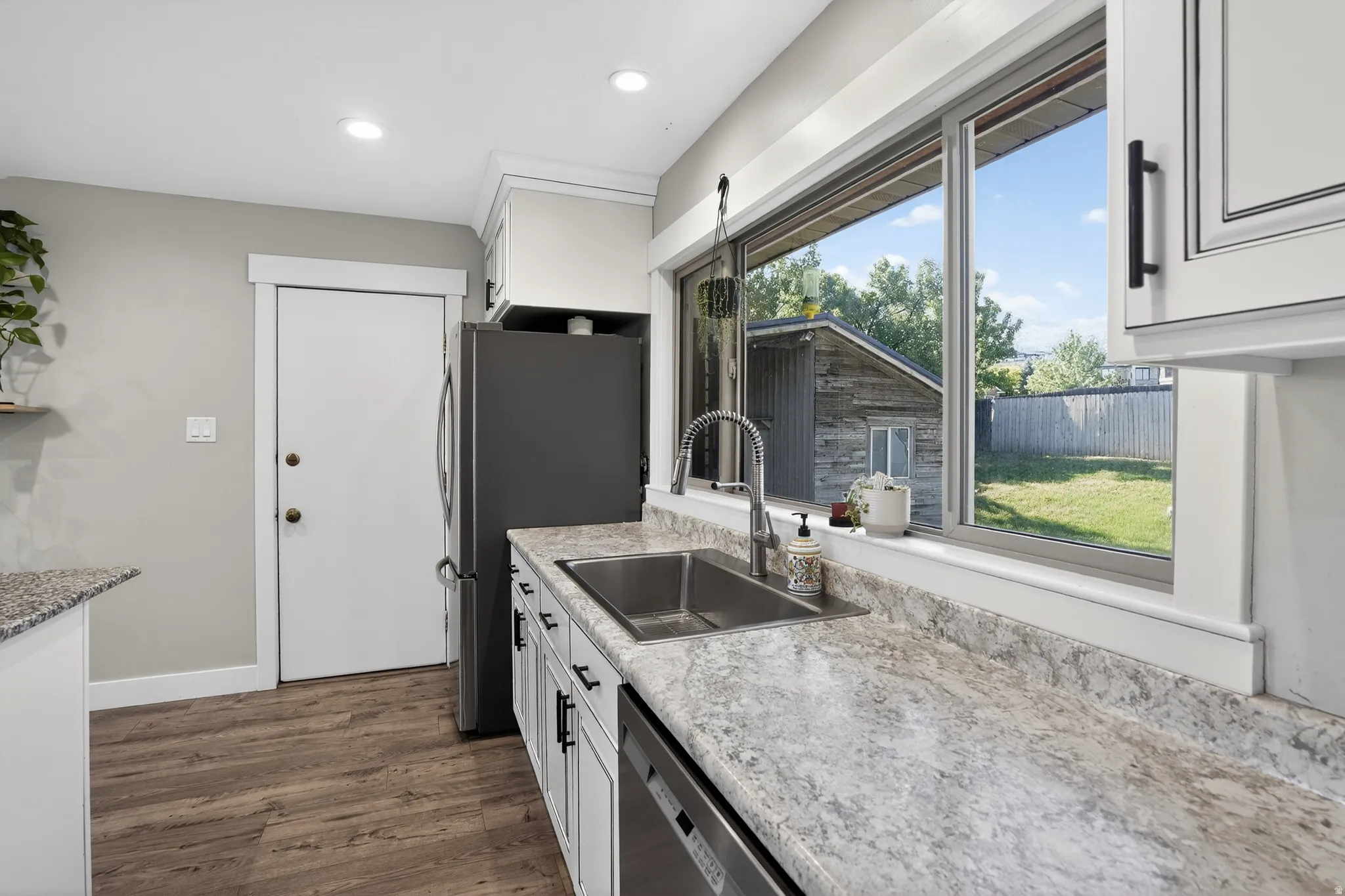 Kitchen featuring light-toned cabinetry with dark hardware, a stainless steel double basin sink with a high-arc faucet, and granite-style countertops