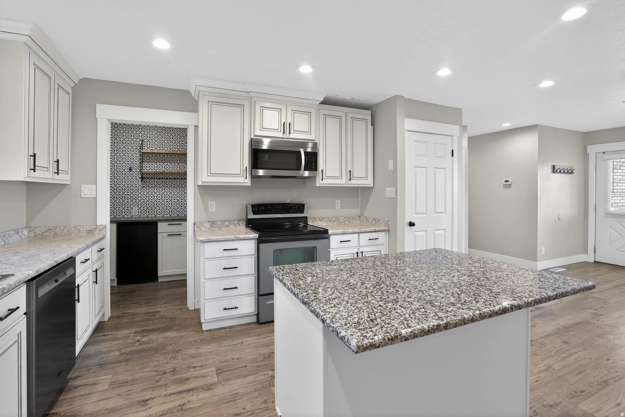 Modern kitchen featuring white cabinetry with dark hardware, granite-style countertops, stainless steel appliances, wood-finish flooring, and recessed lighting