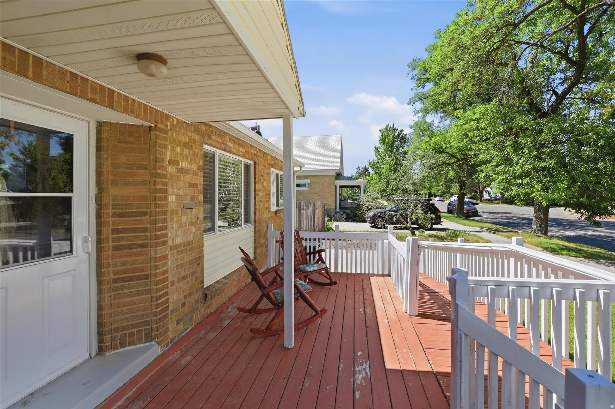Covered front porch featuring a red-stained wooden deck and white wood railing