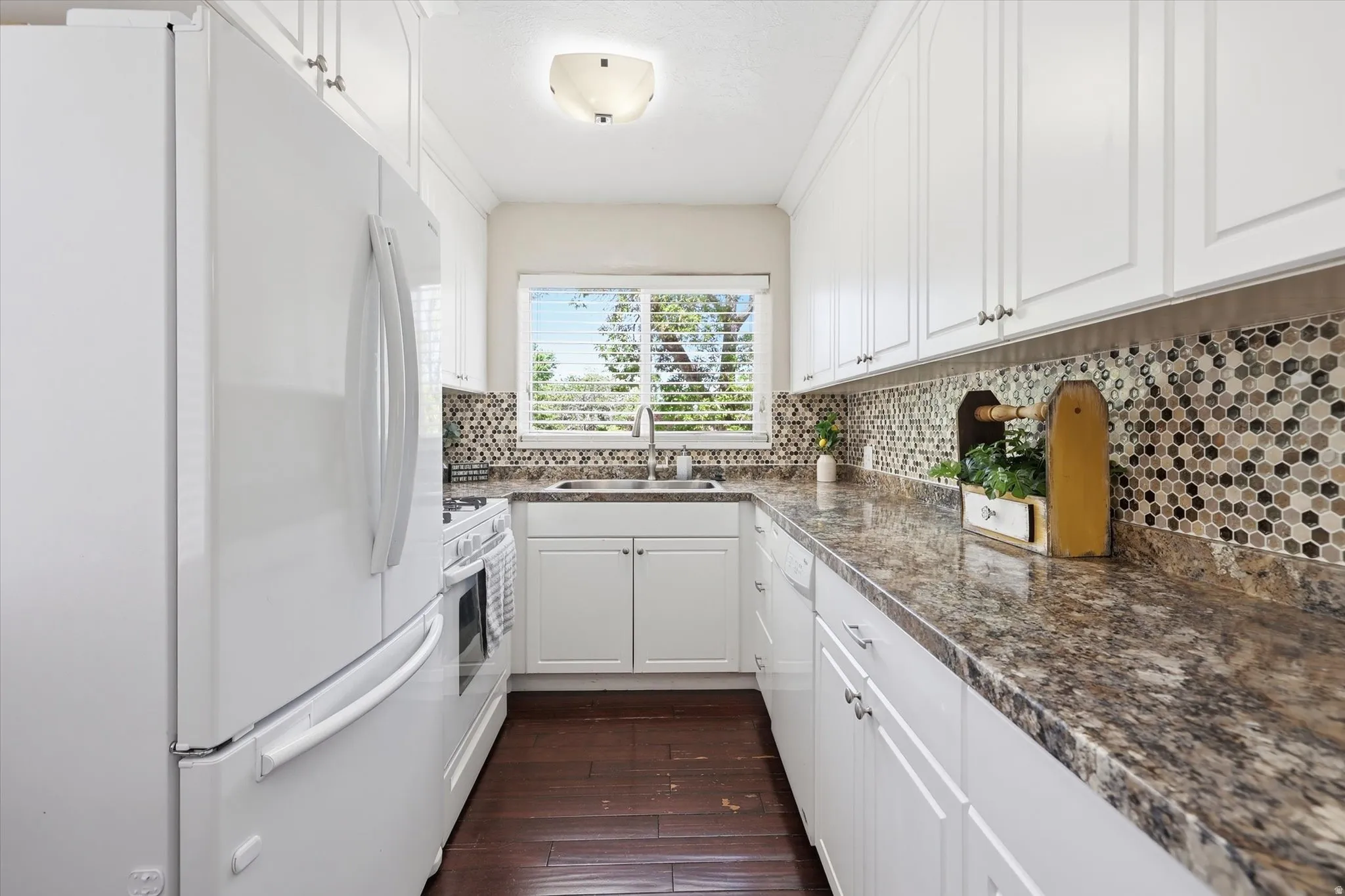 Galley kitchen featuring white cabinetry, a patterned mosaic tile backsplash, solid surface countertops, and wood-finish flooring