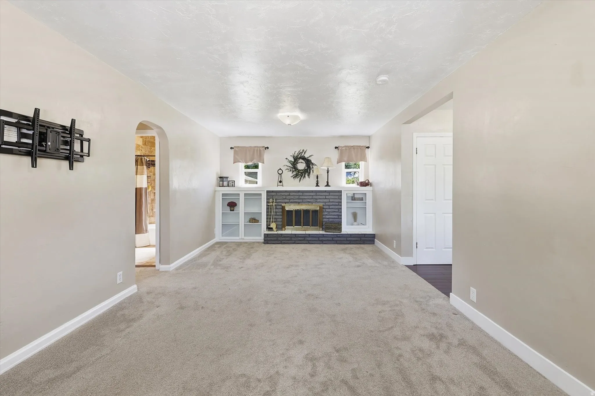 Spacious carpeted room featuring a fireplace with a dark brick surround and a stone hearth