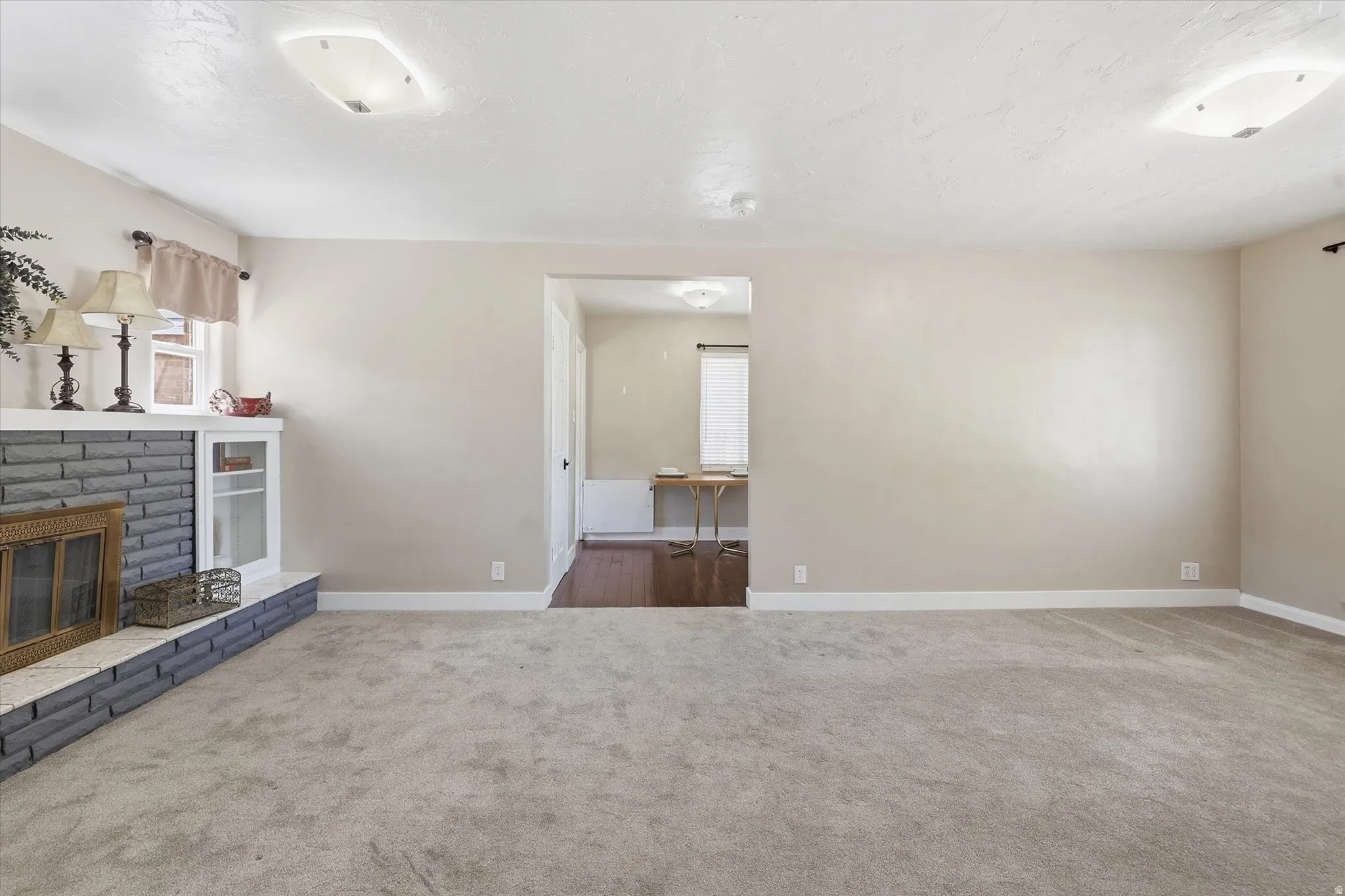 Spacious living area featuring neutral carpeting, a stone-faced fireplace with a white mantle, and a built-in display cabinet
