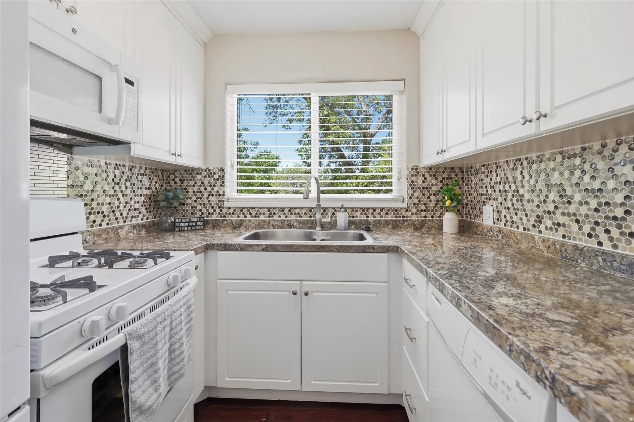 Kitchen featuring white cabinetry with brushed nickel hardware, a stainless steel double basin sink, and a mosaic tile backsplash
