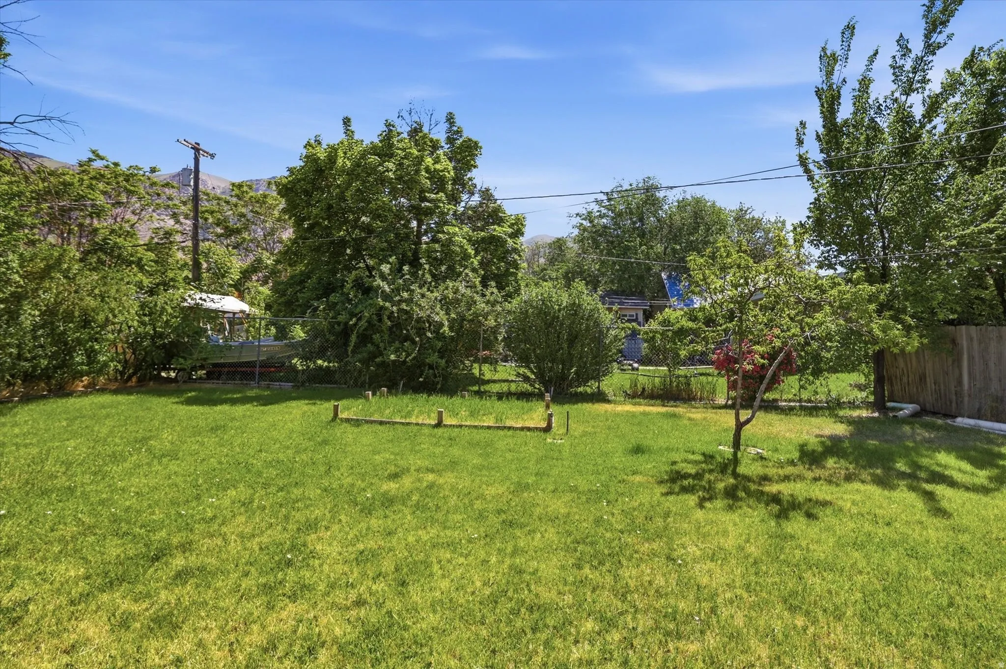 Backyard featuring a lush lawn, mature perimeter trees, partial wood fencing, and a distant mountain backdrop