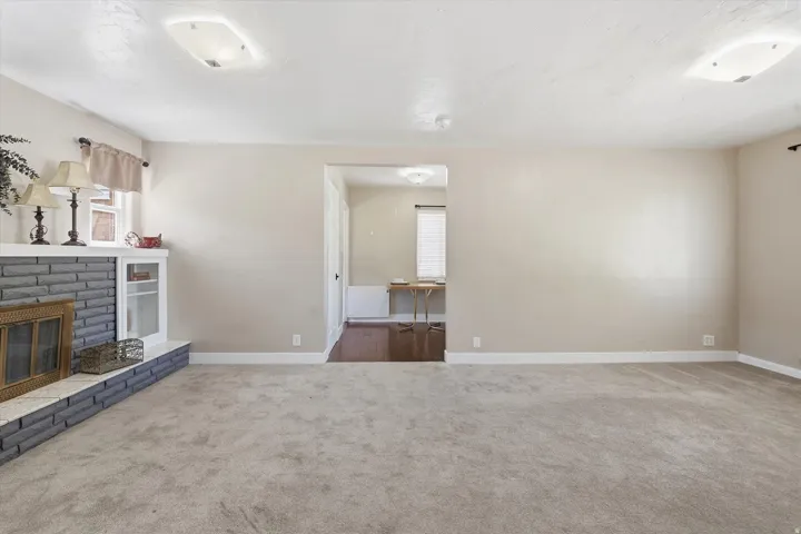 Spacious living area featuring neutral carpeting, a stone-faced fireplace with a white mantle, and a built-in display cabinet