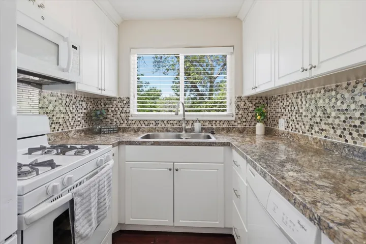 Kitchen featuring white cabinetry with brushed nickel hardware, a stainless steel double basin sink, and a mosaic tile backsplash