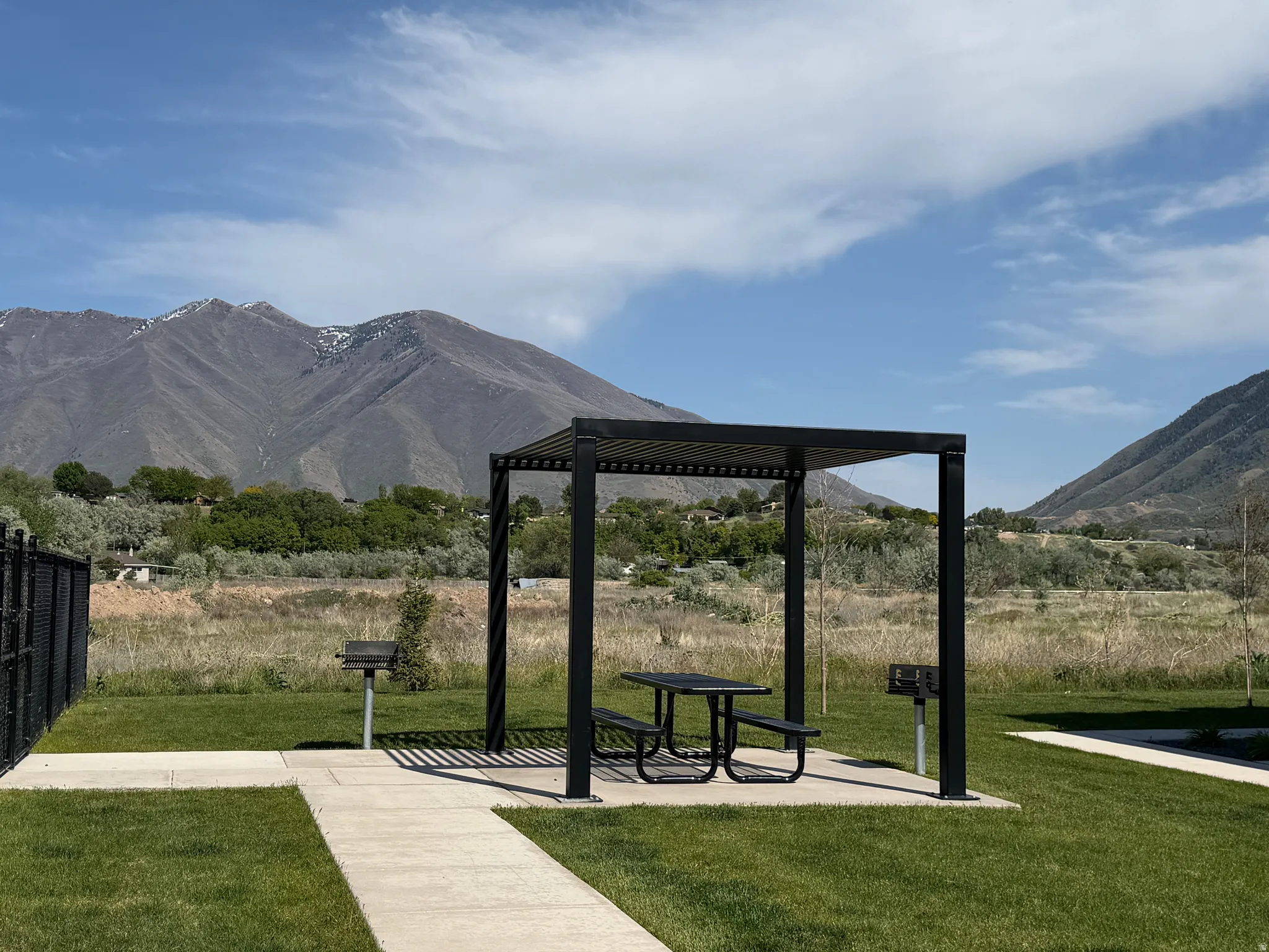 Outdoor amenity area featuring a black metal pergola with a picnic table, two charcoal grills, and manicured lawn