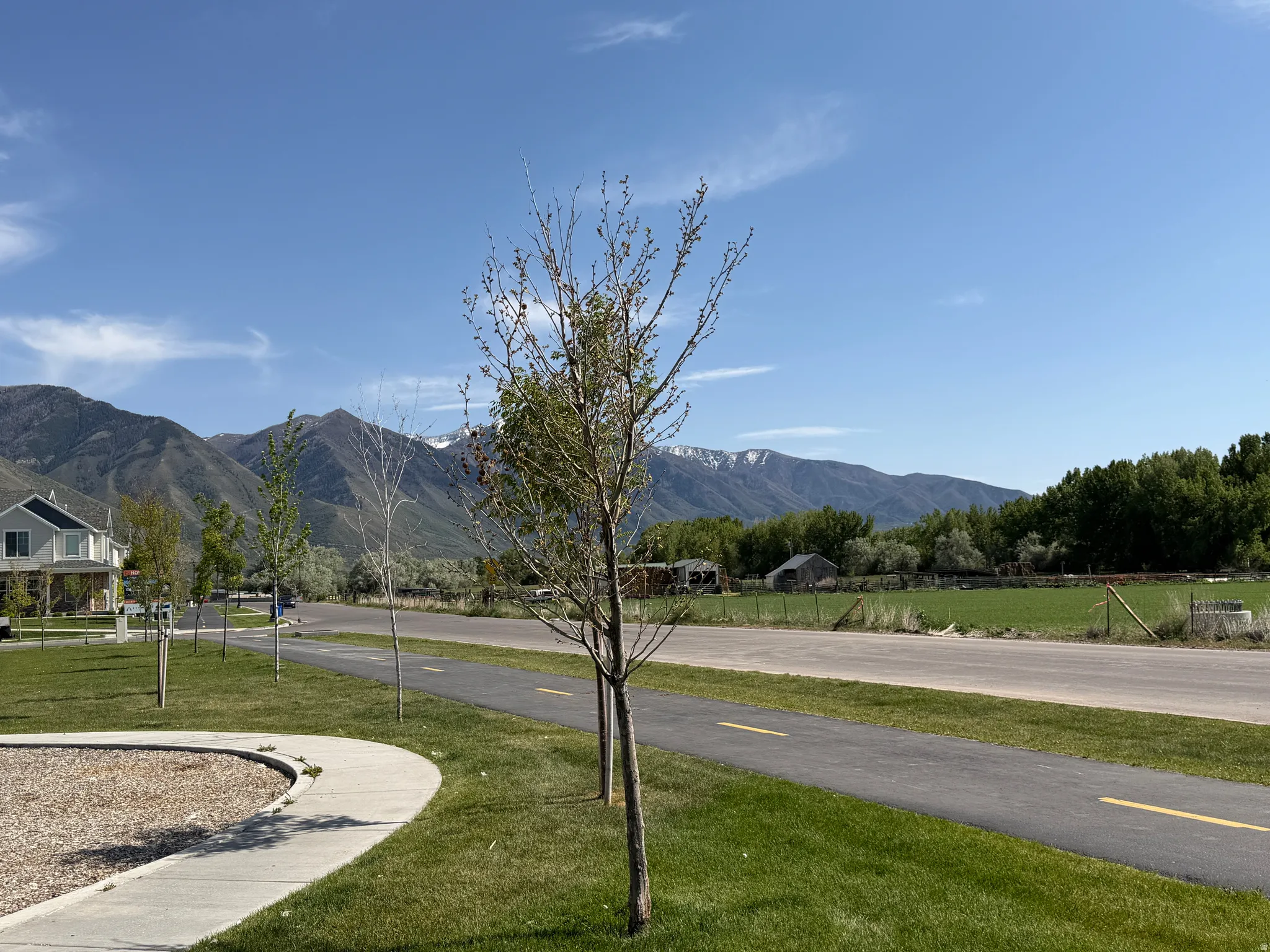 Paved walking path alongside a green space, with distant mountains providing a scenic backdrop
