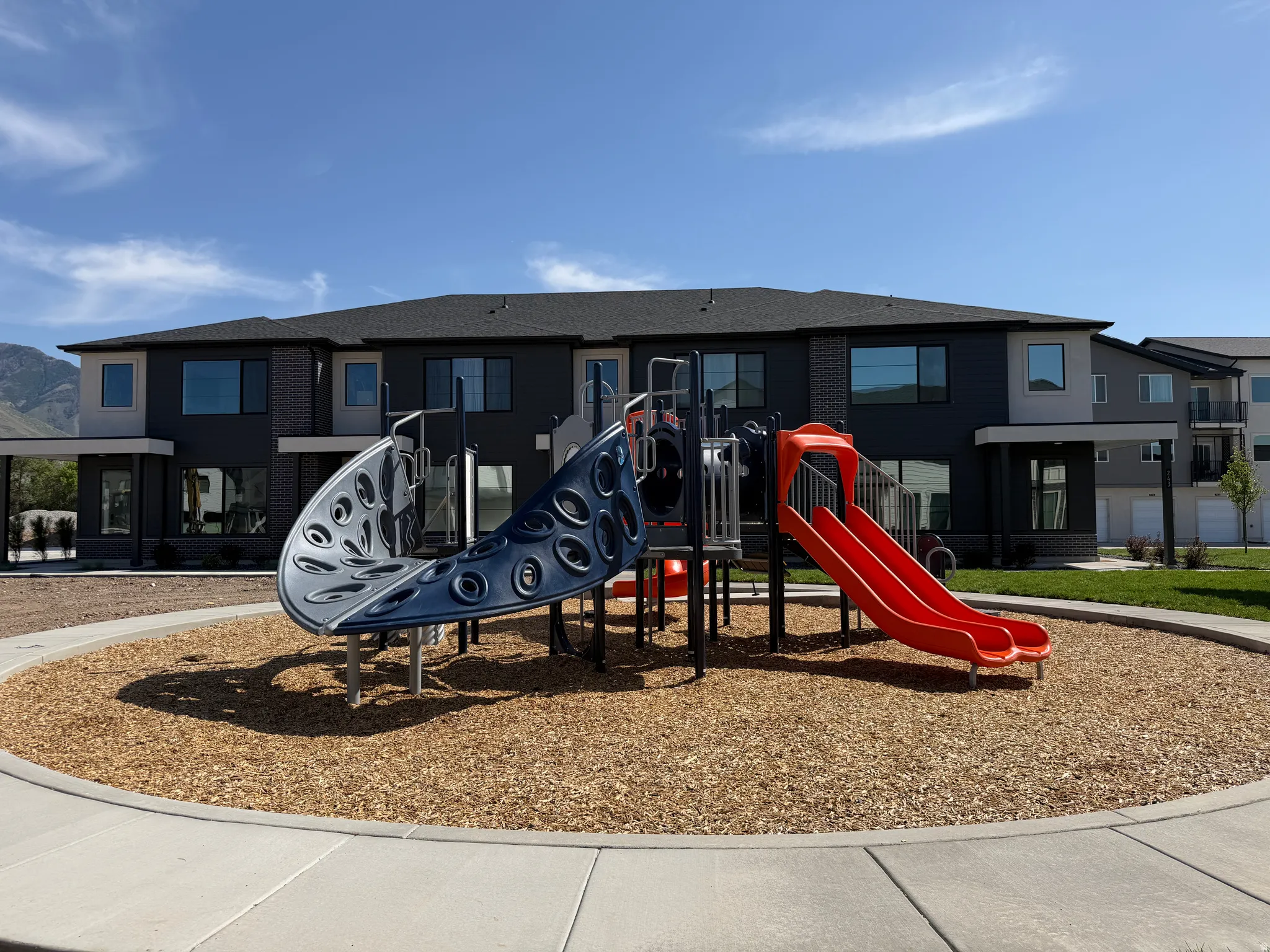 Community playground featuring a multi-level play structure with slides and climbing elements, set on a wood chip surface