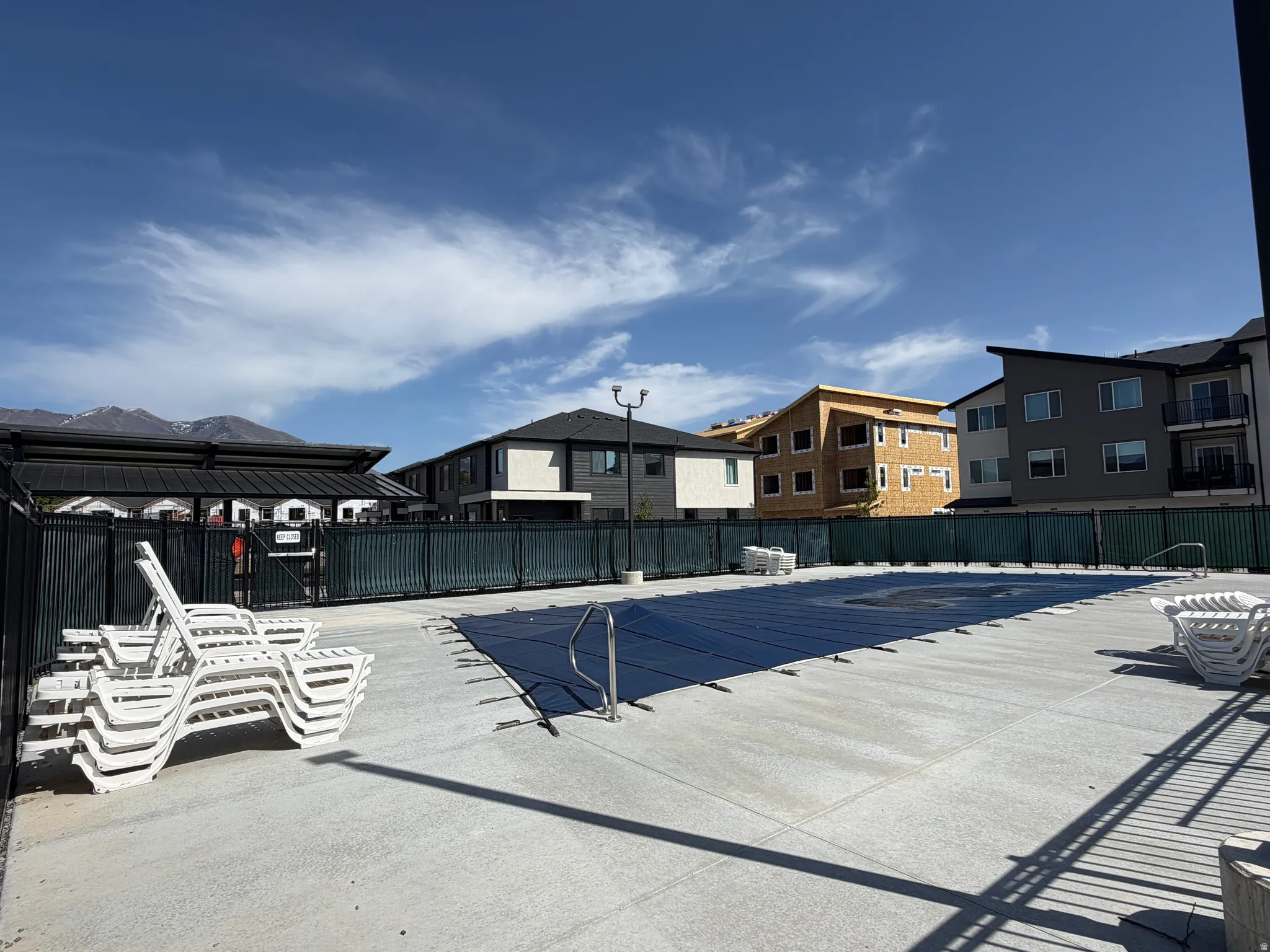 Community pool area featuring a covered pool, concrete decking, and perimeter fencing