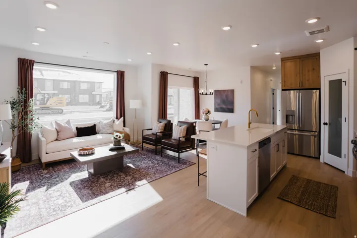 Open-concept living space featuring wood-finish flooring, recessed lighting, and a prominent kitchen island with a gold-tone faucet
