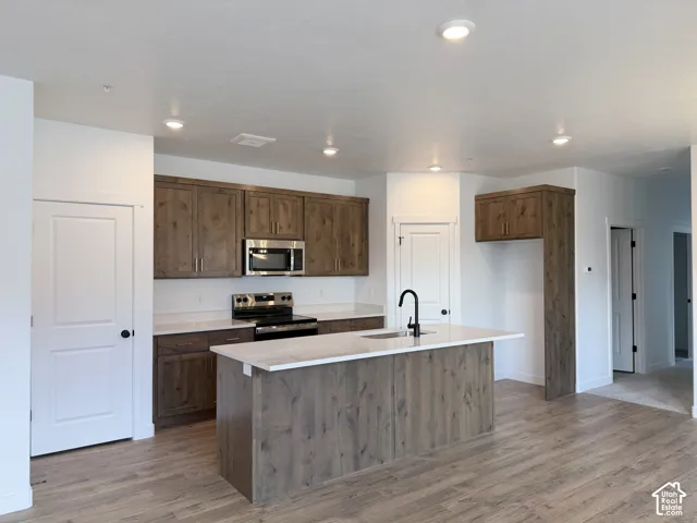 Kitchen featuring wood-finish cabinetry, stainless steel appliances, a center island with sink, and light-toned countertops