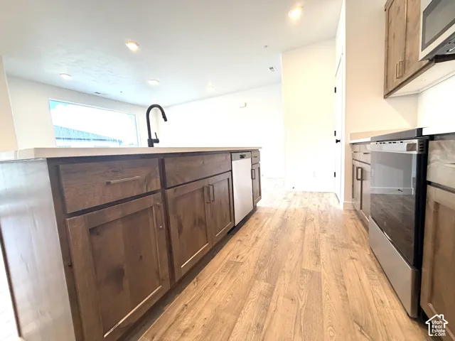 Kitchen featuring wood-finish flooring, an island with integrated sink, stainless steel appliances, and recessed ceiling lighting