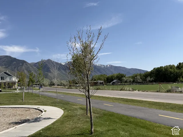 Paved walking path alongside a green space, with distant mountains providing a scenic backdrop