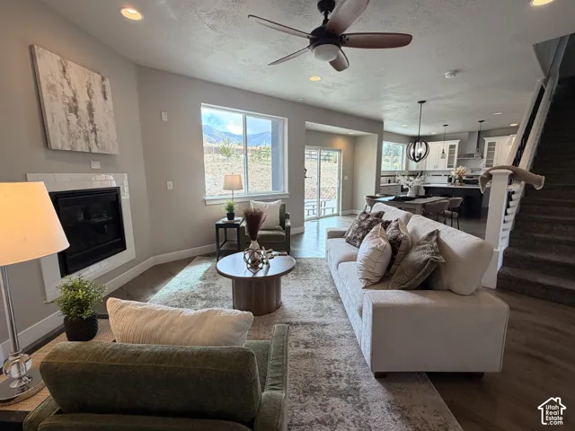 Contemporary open-concept living area with a fireplace featuring white subway tile surround, recessed lighting, wood-finish flooring, and a ceiling fan