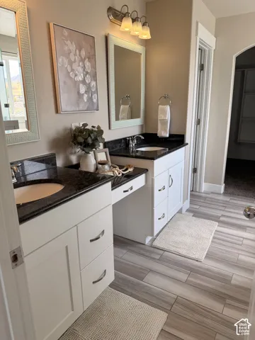 Dual vanity with dark stone countertops, white cabinetry, undermount sinks, and plank-style flooring