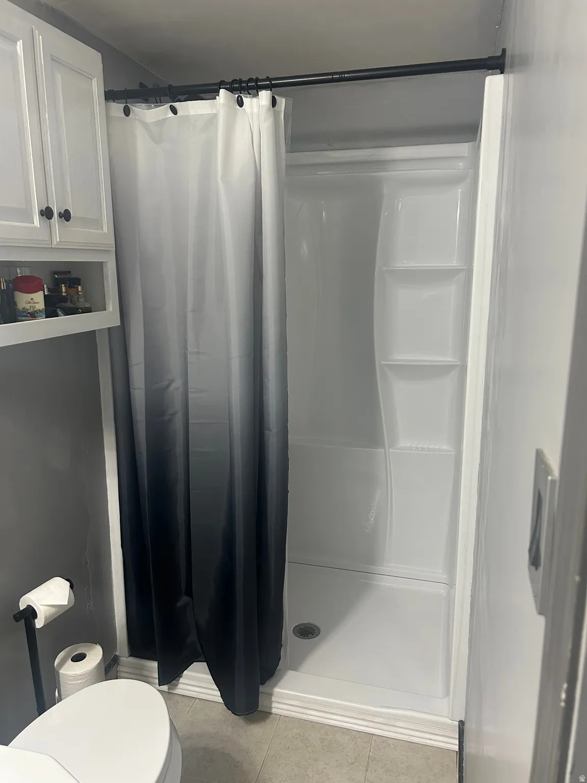 Fiberglass shower stall with integrated shelving and a white base, complemented by a black shower rod