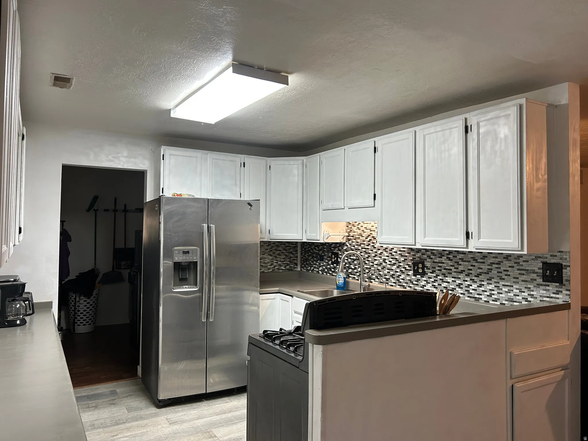 Kitchen featuring white cabinetry, grey countertops, stainless steel appliances, mosaic tile backsplash, and wood-finish flooring