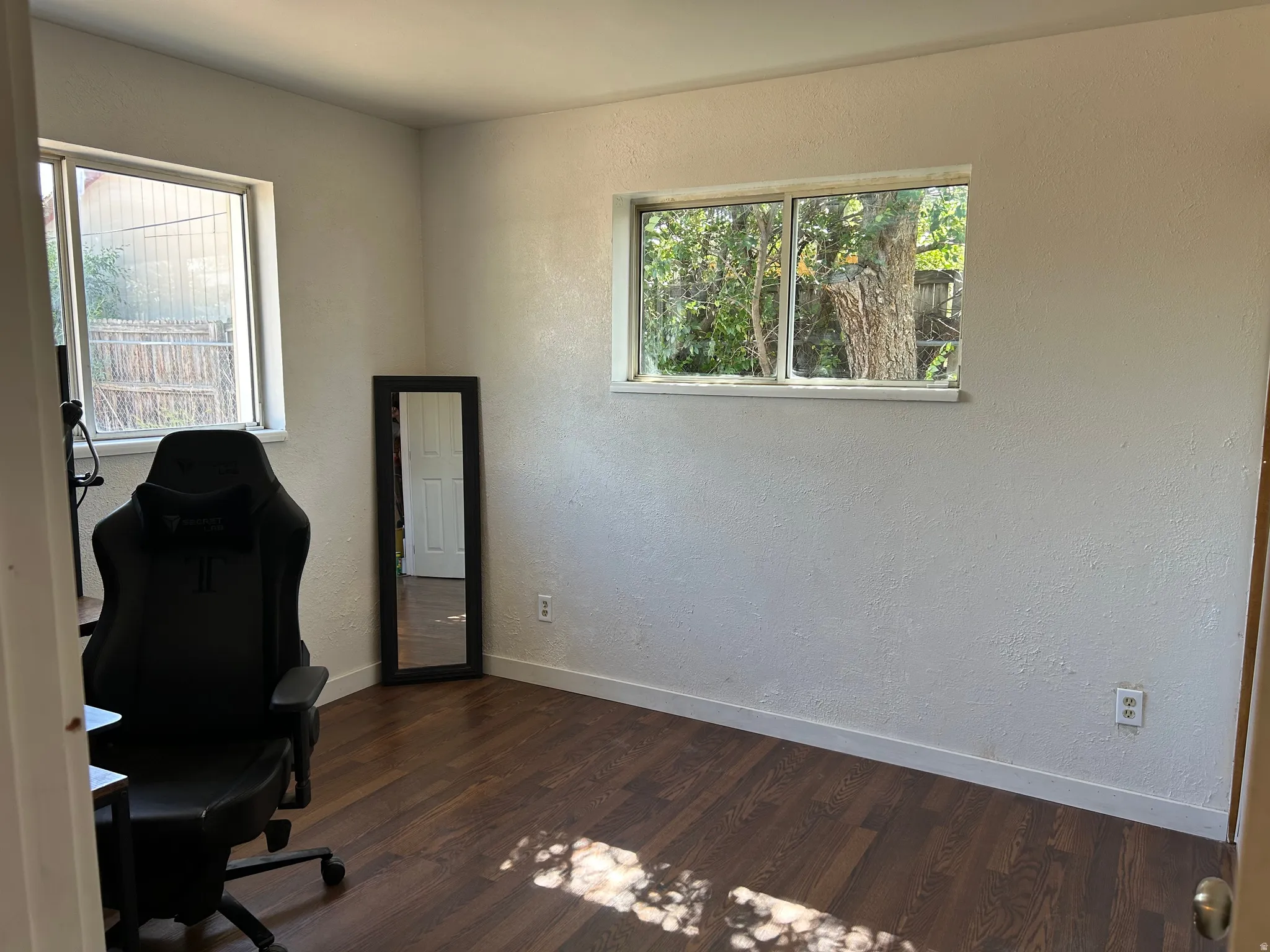 Bright room featuring wood-finish flooring, white painted walls, and two windows providing natural light
