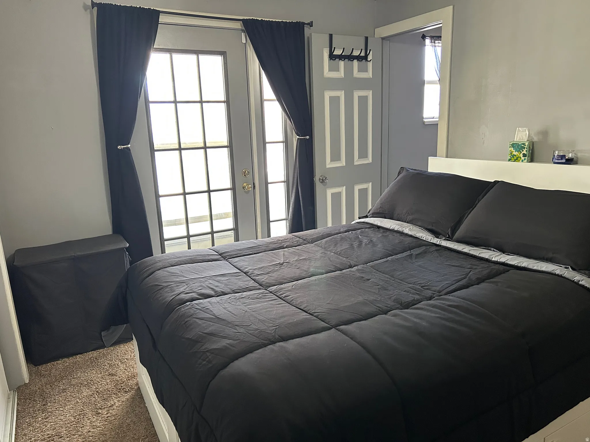 Bedroom featuring a glass-paneled door with black curtains, wall-to-wall carpeting, and a white headboard