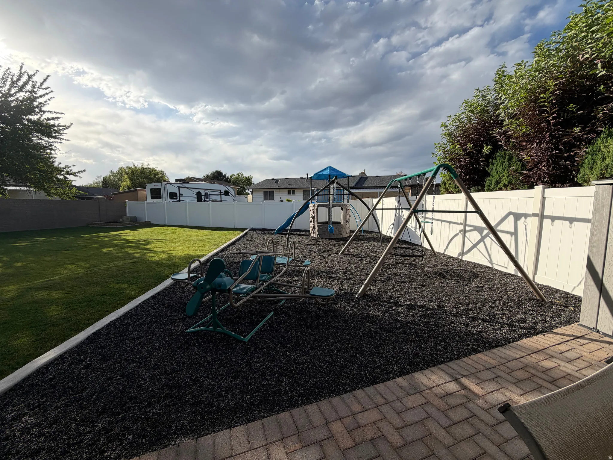 Expansive backyard featuring a large lawn area, a dedicated play area with dark ground covering, and a white privacy fence