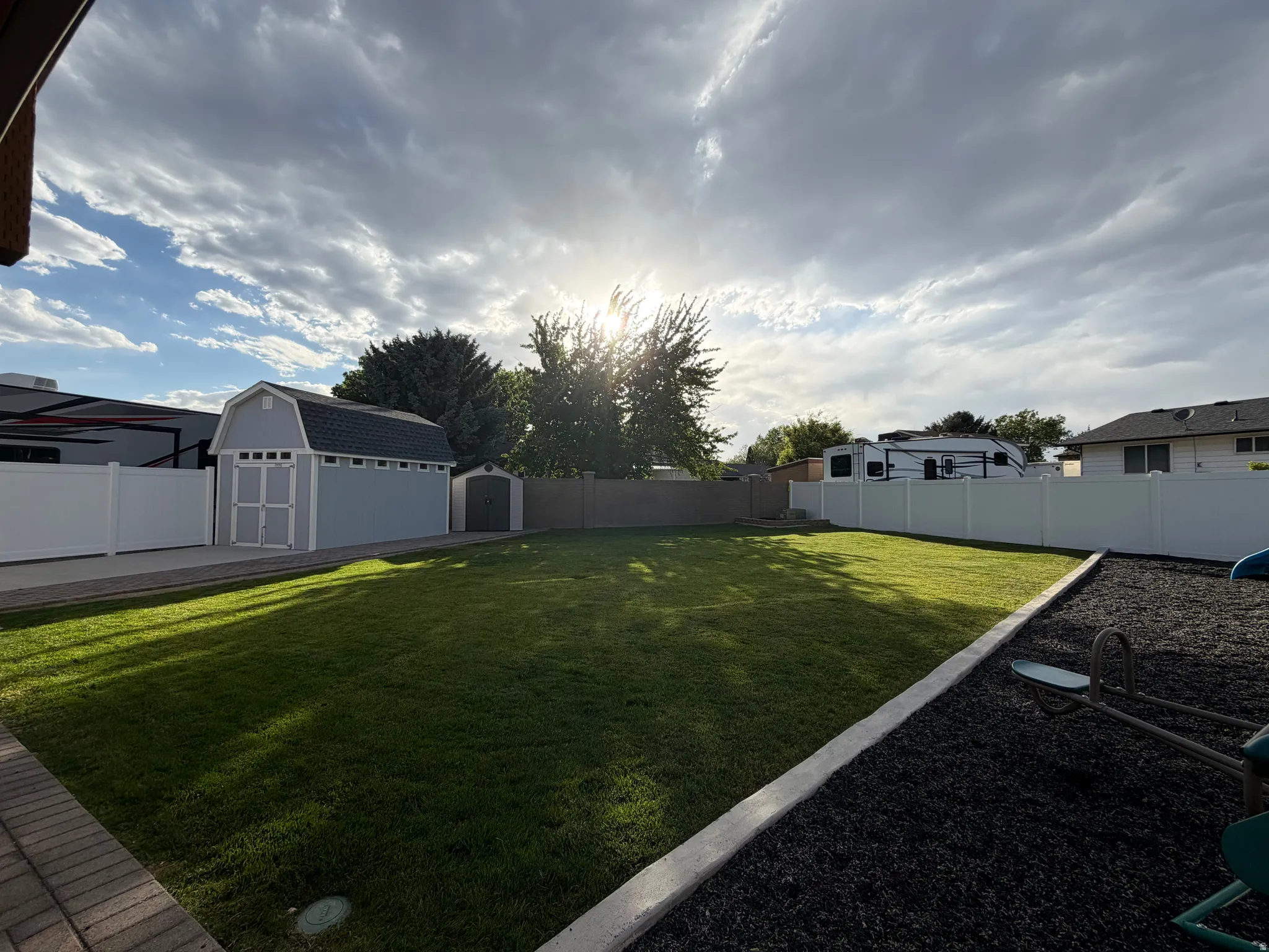 Expansive backyard featuring a manicured lawn, a large light blue storage shed with a dark roof, a smaller secondary shed, and a white vinyl privacy fence