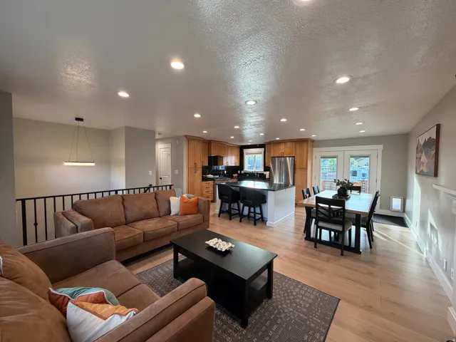 Open-concept living space featuring wood-finish flooring, recessed lighting, and a modern kitchen with natural wood cabinetry and black countertops