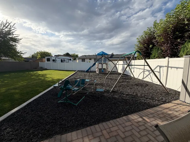 Expansive backyard featuring a large lawn area, a dedicated play area with dark ground covering, and a white privacy fence