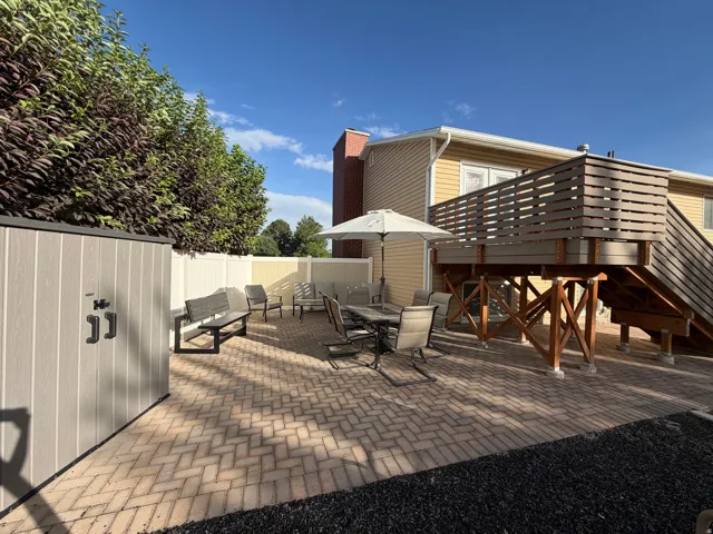 Expansive brick paver patio featuring a multi-level wood deck with slatted railing, privacy fencing, and a detached storage shed