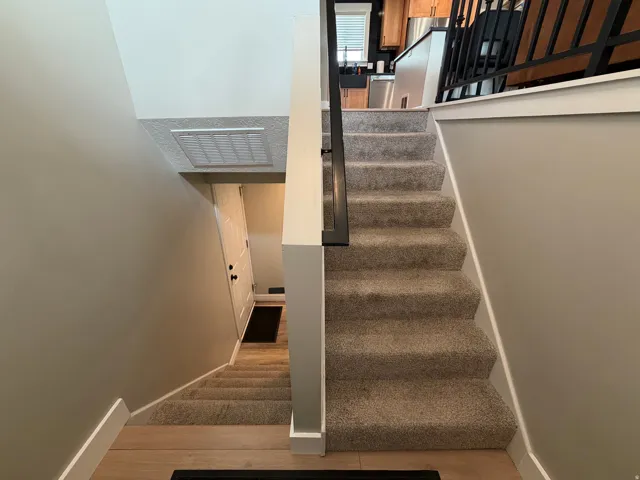 Split-level staircase featuring carpeted treads, a black metal railing, and light wood-finish flooring at the base
