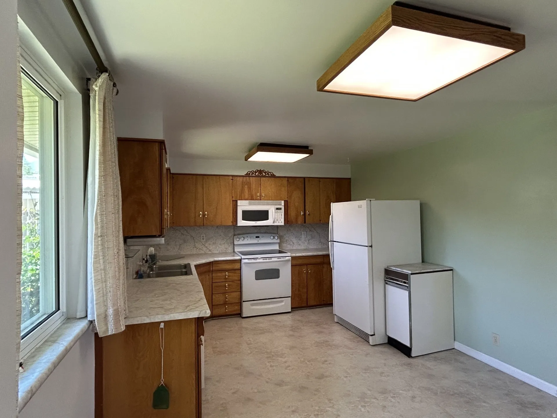 Kitchen featuring wood cabinetry, white appliances, light-toned flooring, & a large window.