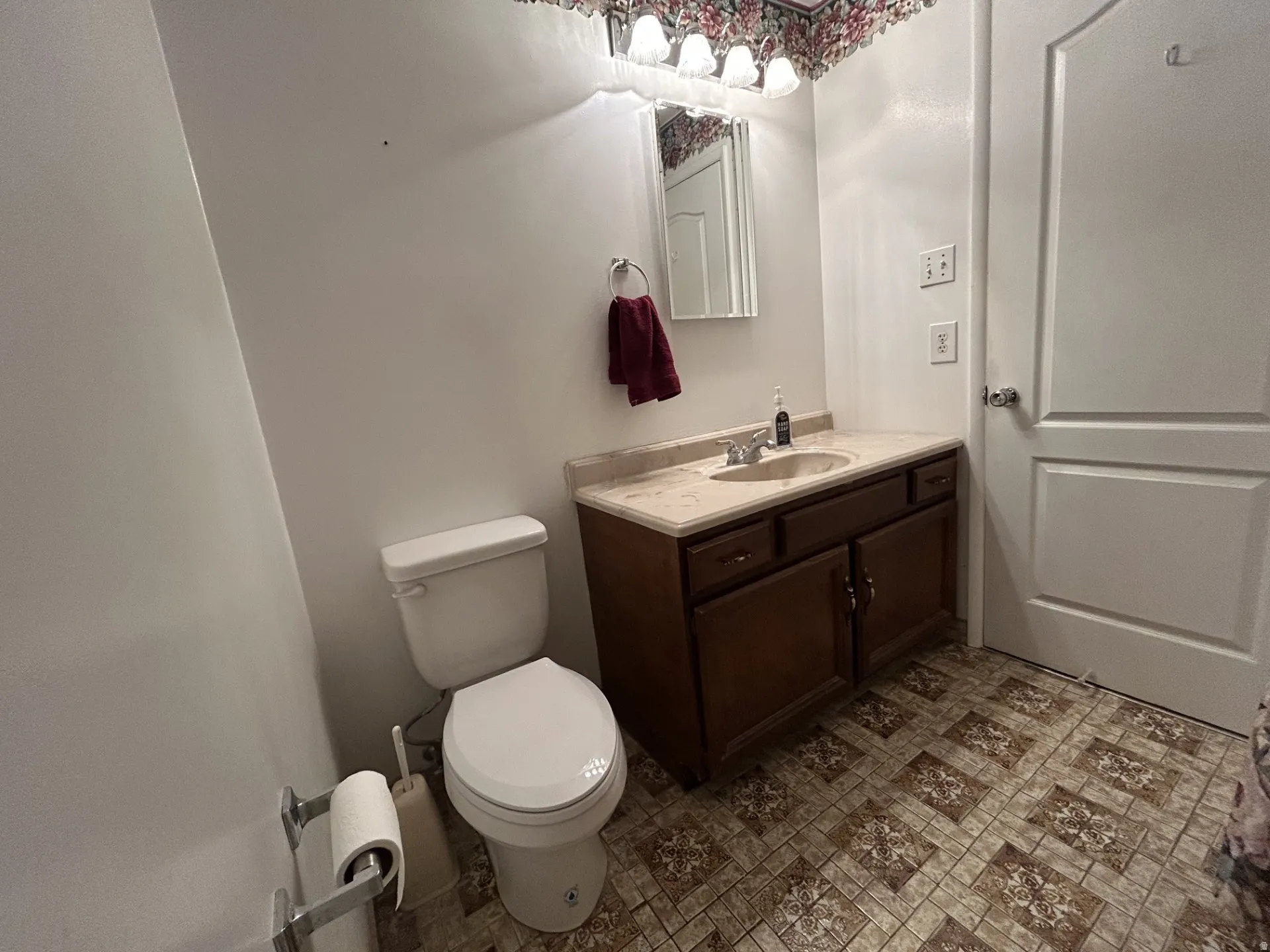Main Full Bathroom featuring a vanity with a light-colored countertop, a built-in sink, a dark wood-finish cabinet & vinyl flooring.