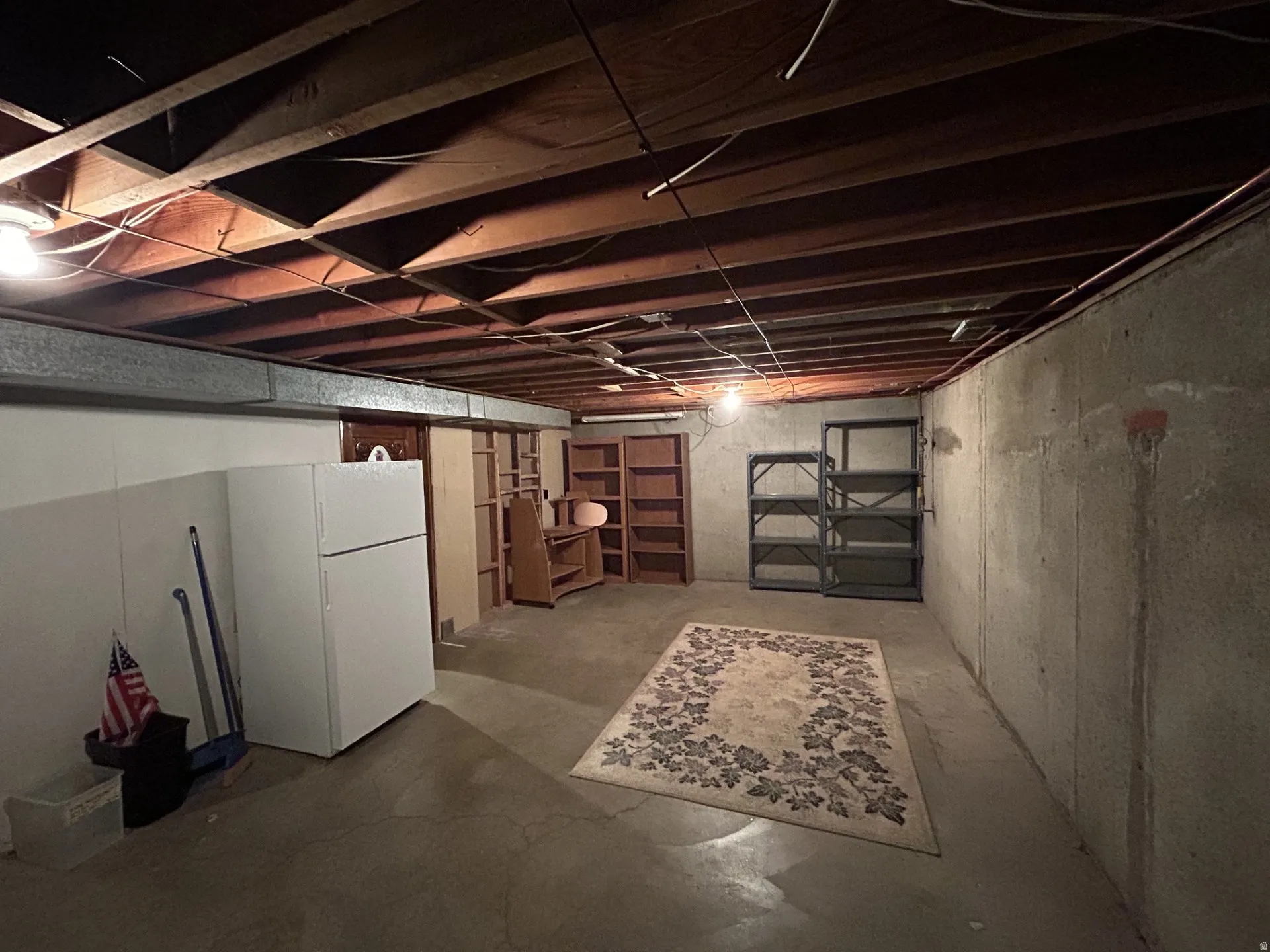 Unfinished basement featuring wood ceiling joists & concrete flooring. 2nd refrigerator included in transaction.