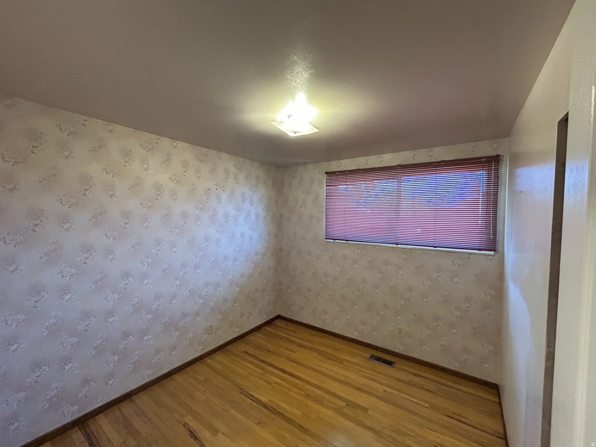 2nd bedroom featuring wood flooring, patterned wallpaper, a window with horizontal blinds, and a ceiling-mounted light fixture