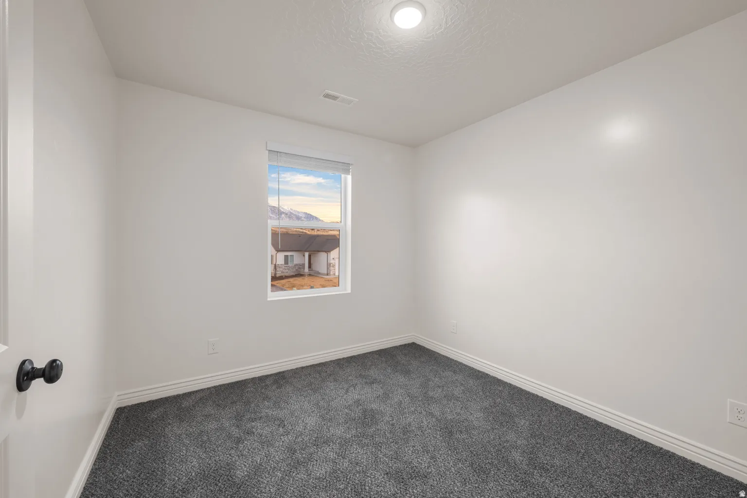 Compact room featuring dark gray carpeting, crisp white walls, and a single window
