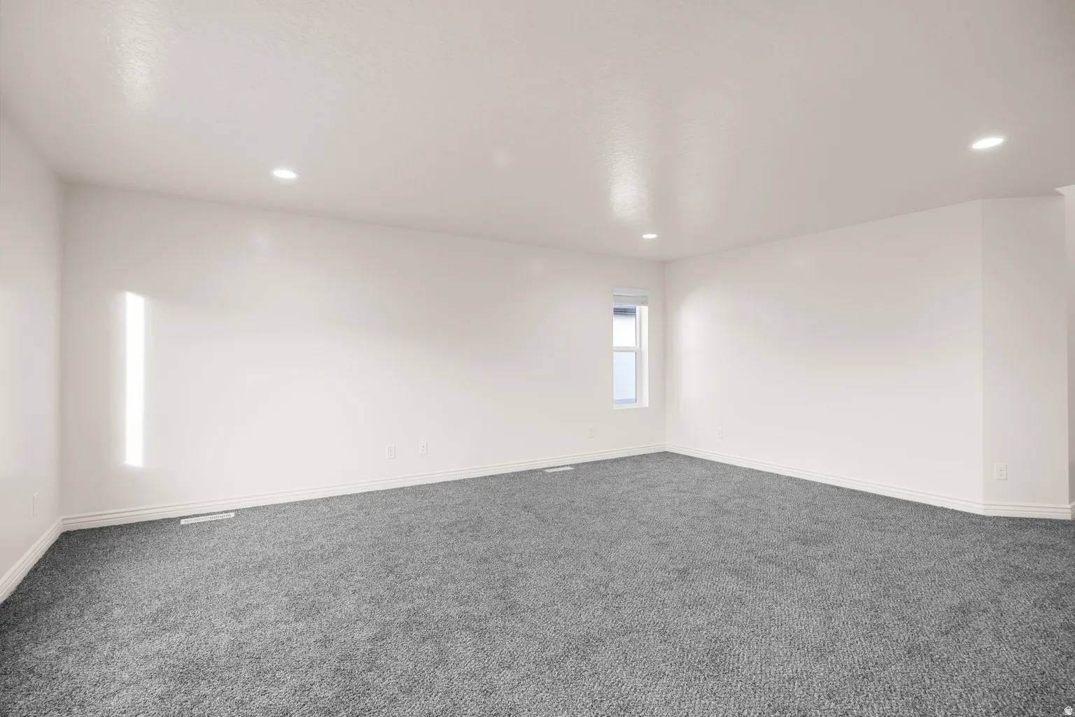 Spacious room featuring neutral carpeting, white wall paint, and recessed ceiling lighting
