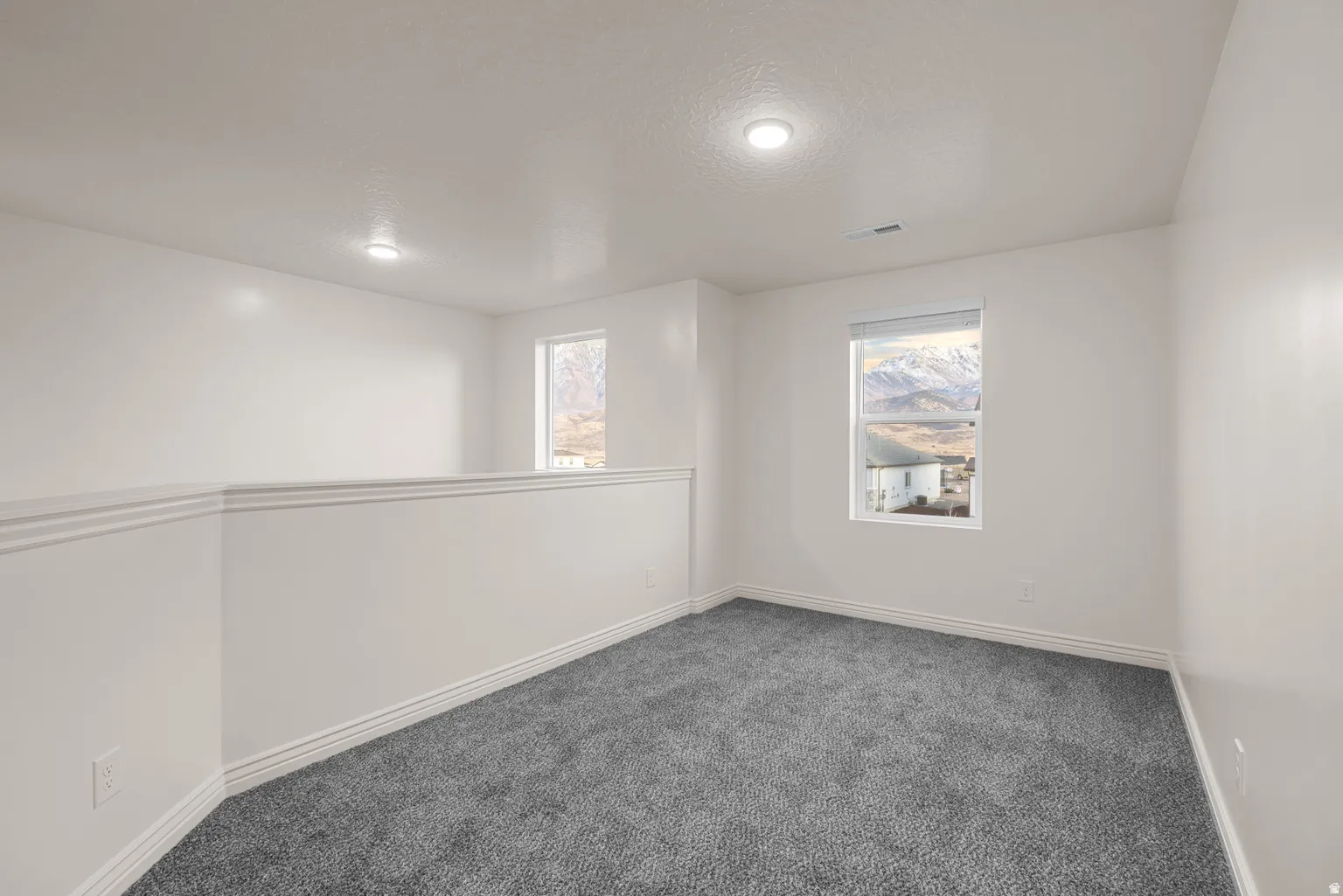 Carpeted loft space featuring bright white walls, recessed lighting, and a half-wall partition with decorative trim