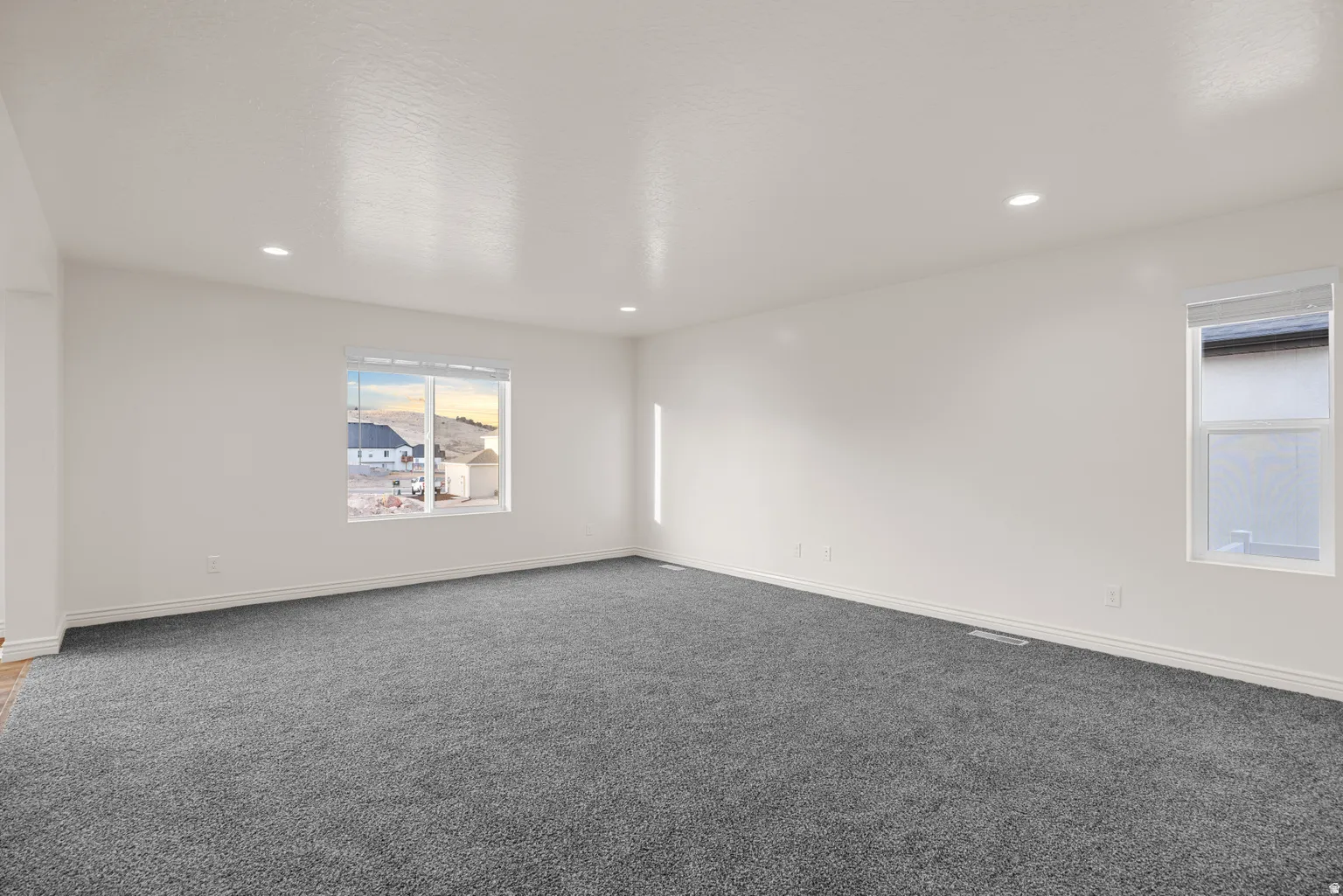 Spacious interior room featuring plush gray carpeting, white painted walls, recessed lighting, and white baseboards