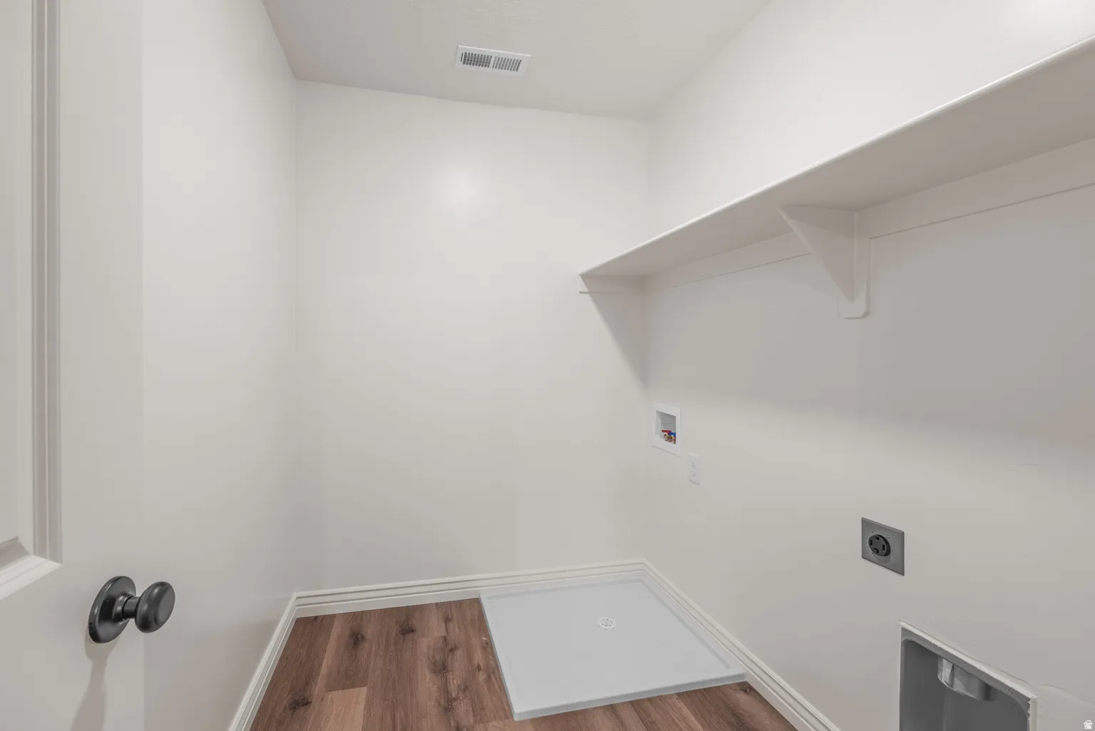 Dedicated laundry area featuring a white wall shelf, wood-finish flooring, and white baseboards