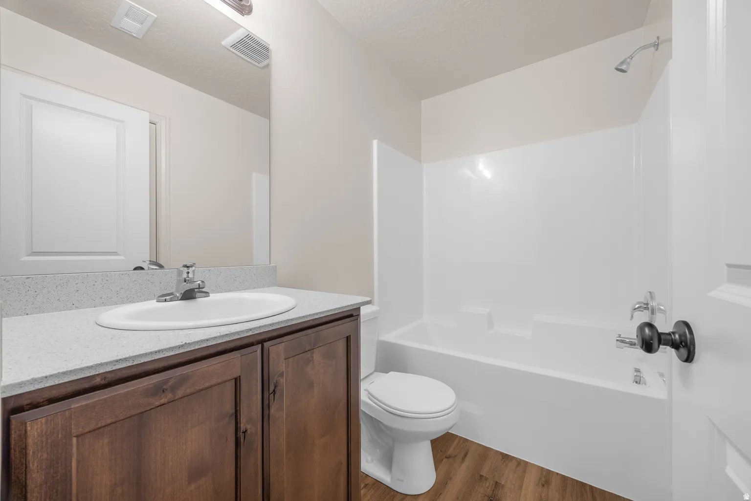 Bathroom featuring a dark wood-finish vanity with a light speckled countertop, an undermount sink, and a white shower-over-tub combination with a single-handle faucet