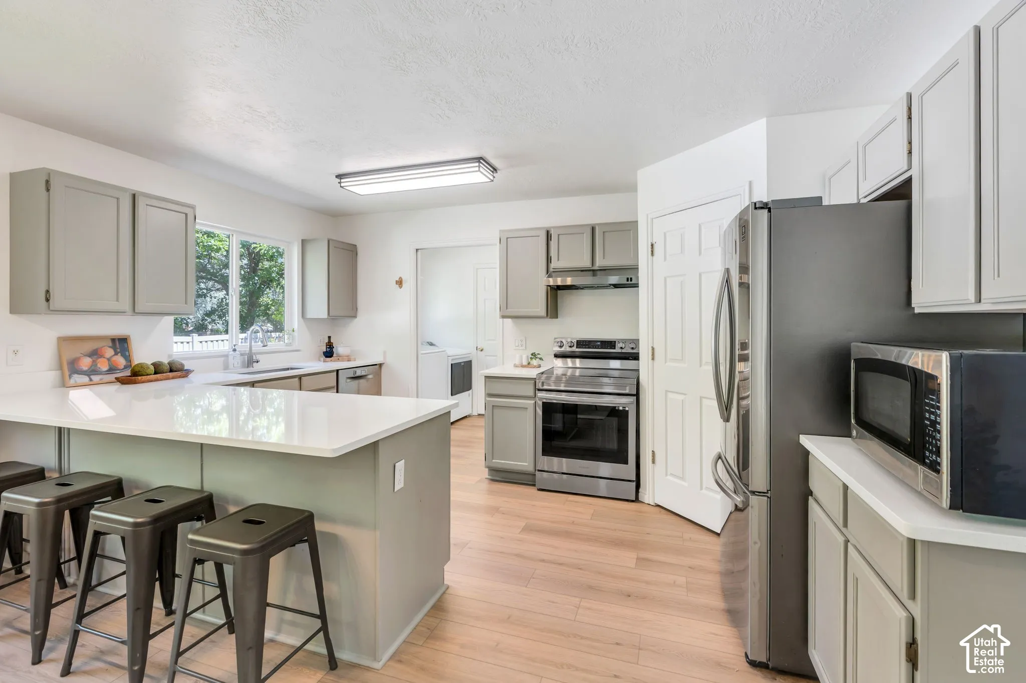 Modern kitchen featuring light wood-finish flooring, white countertops, and gray cabinetry