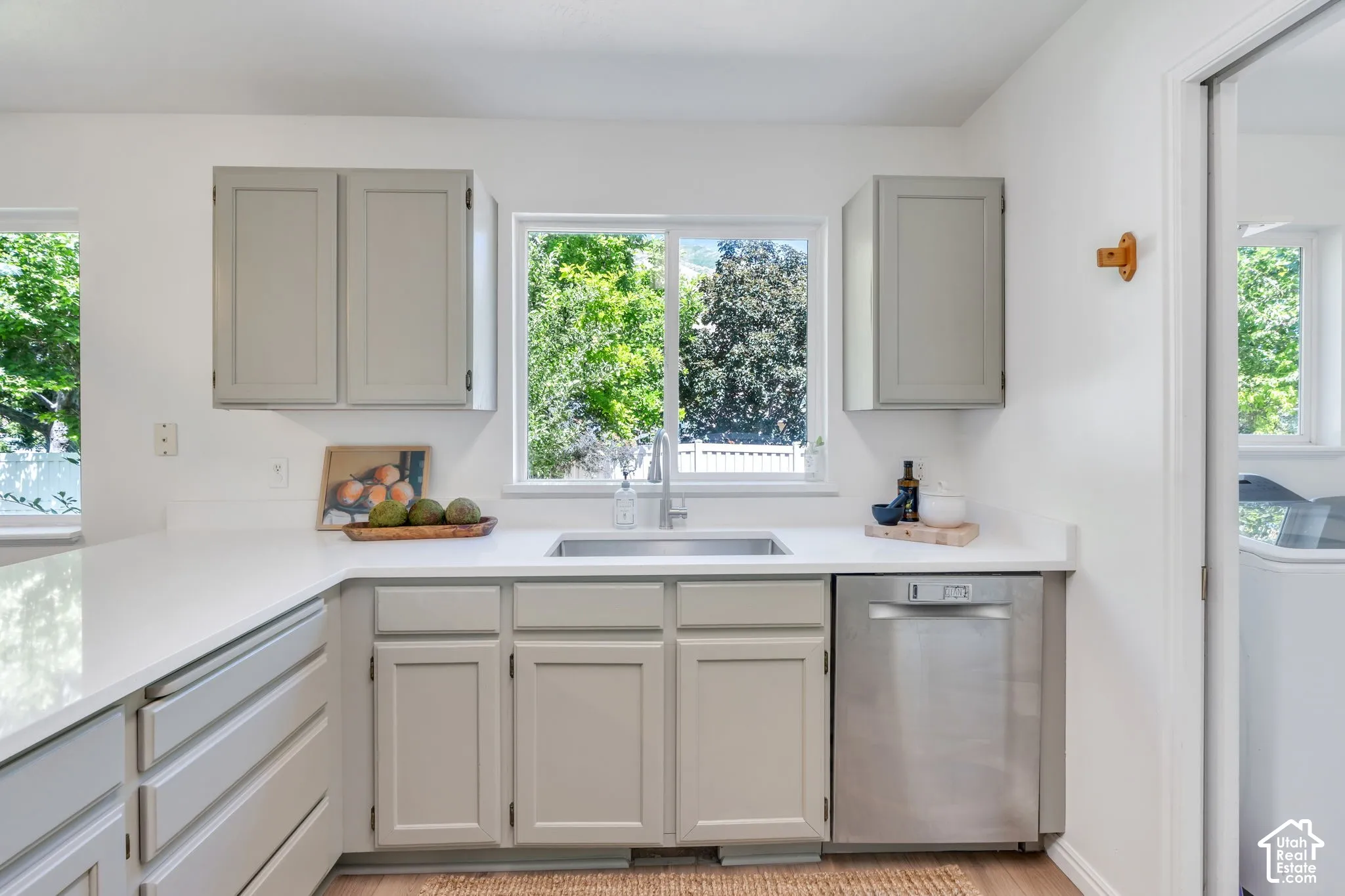 Kitchen featuring light gray cabinetry, white countertops, a stainless steel sink, and a stainless steel dishwasher