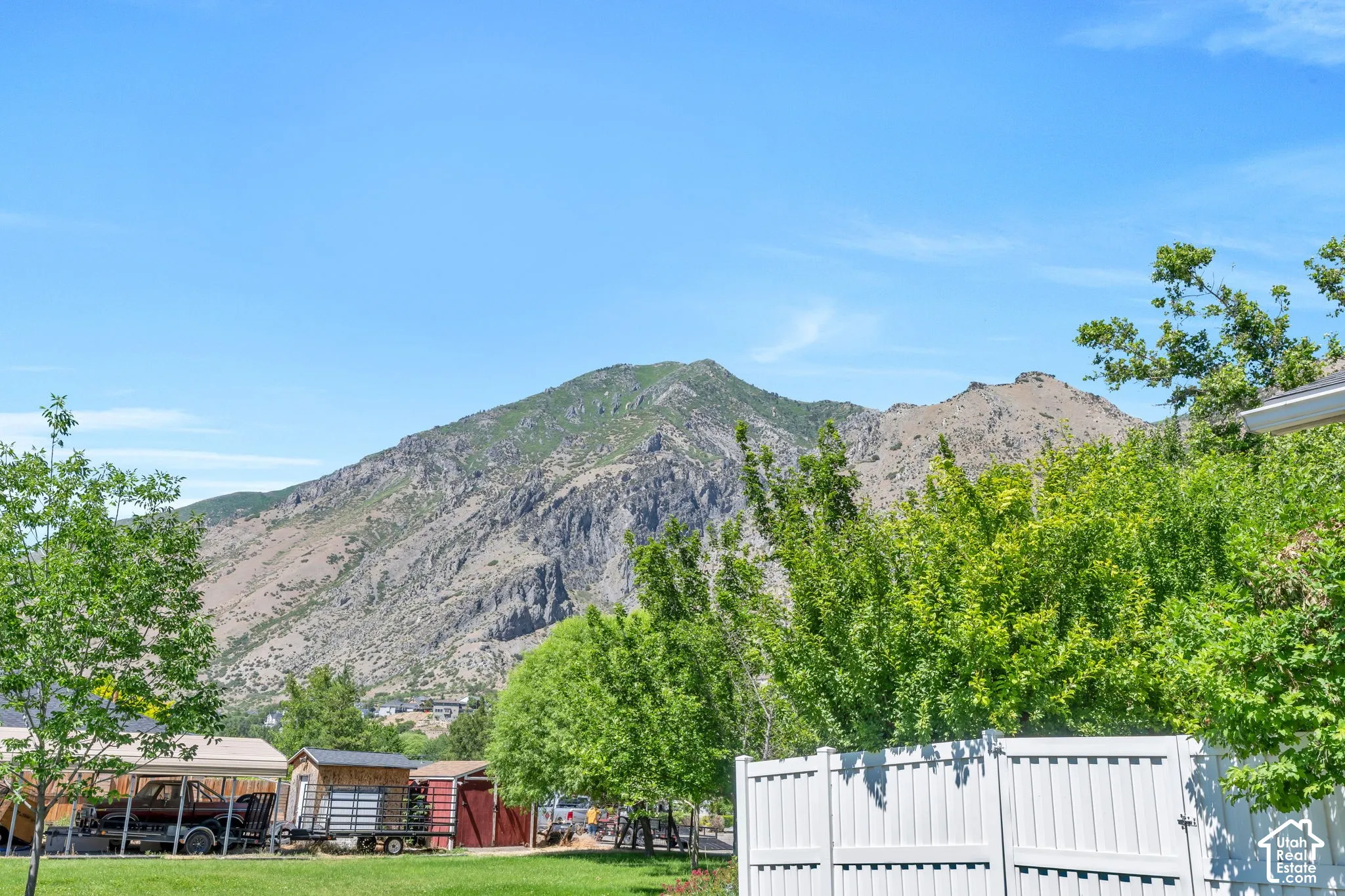 Mountain backdrop with a clear sky, featuring a white vinyl fence and mature green trees