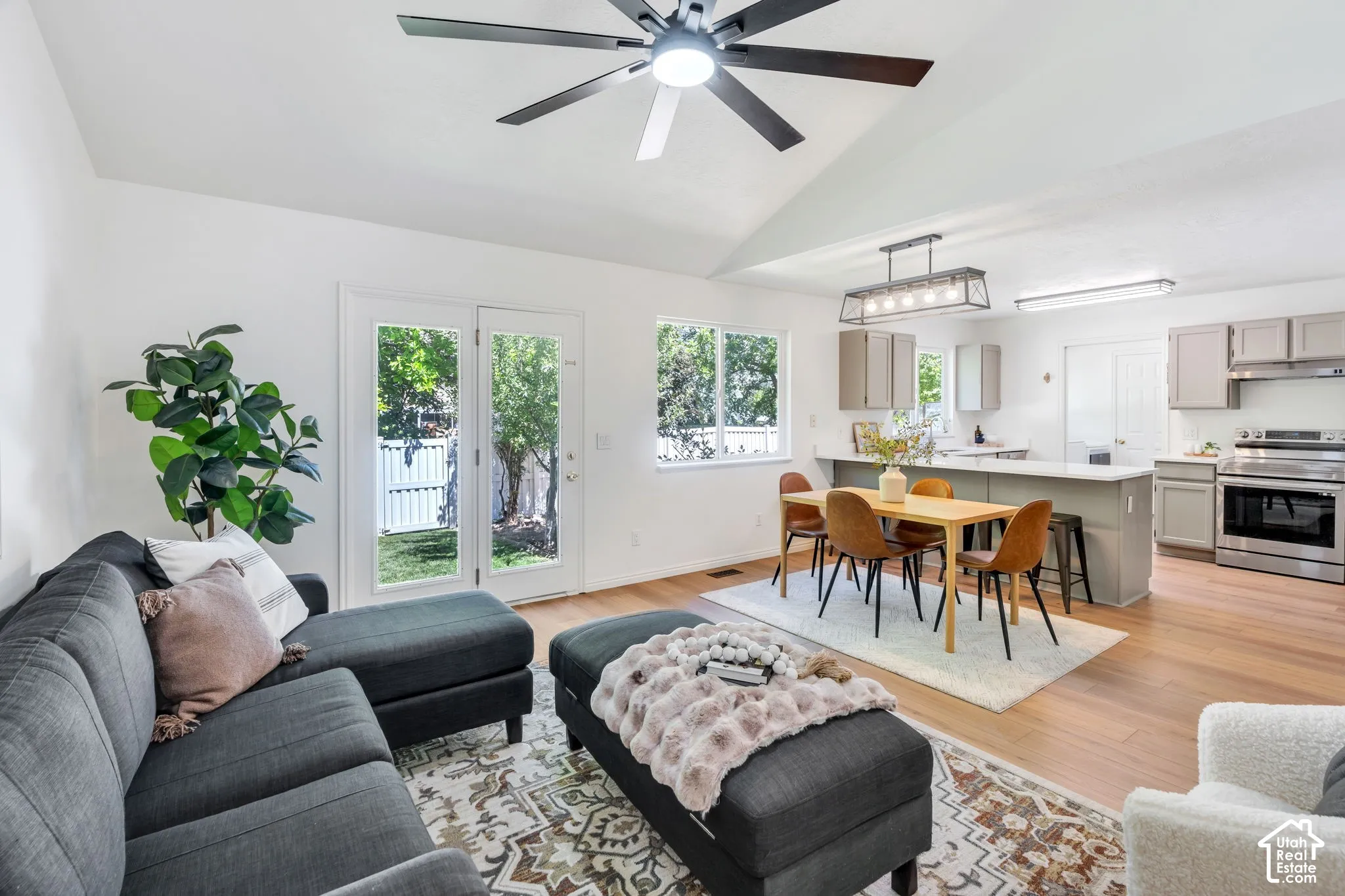Spacious open-concept living area featuring a vaulted ceiling with a modern ceiling fan, wood-finish flooring, and white walls