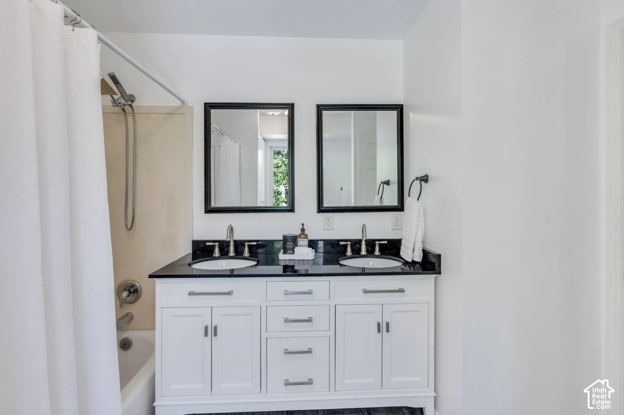 Bathroom featuring a dual vanity with white cabinetry, black countertops, and undermount sinks